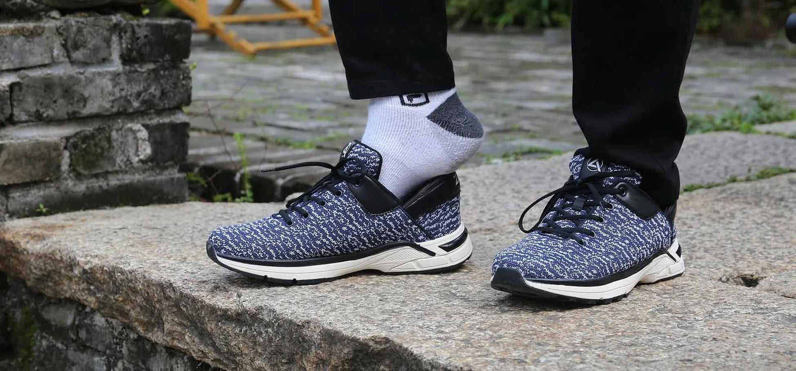 A pair of navy knit Zeba hands-free sneakers being worn with white socks on a stone step